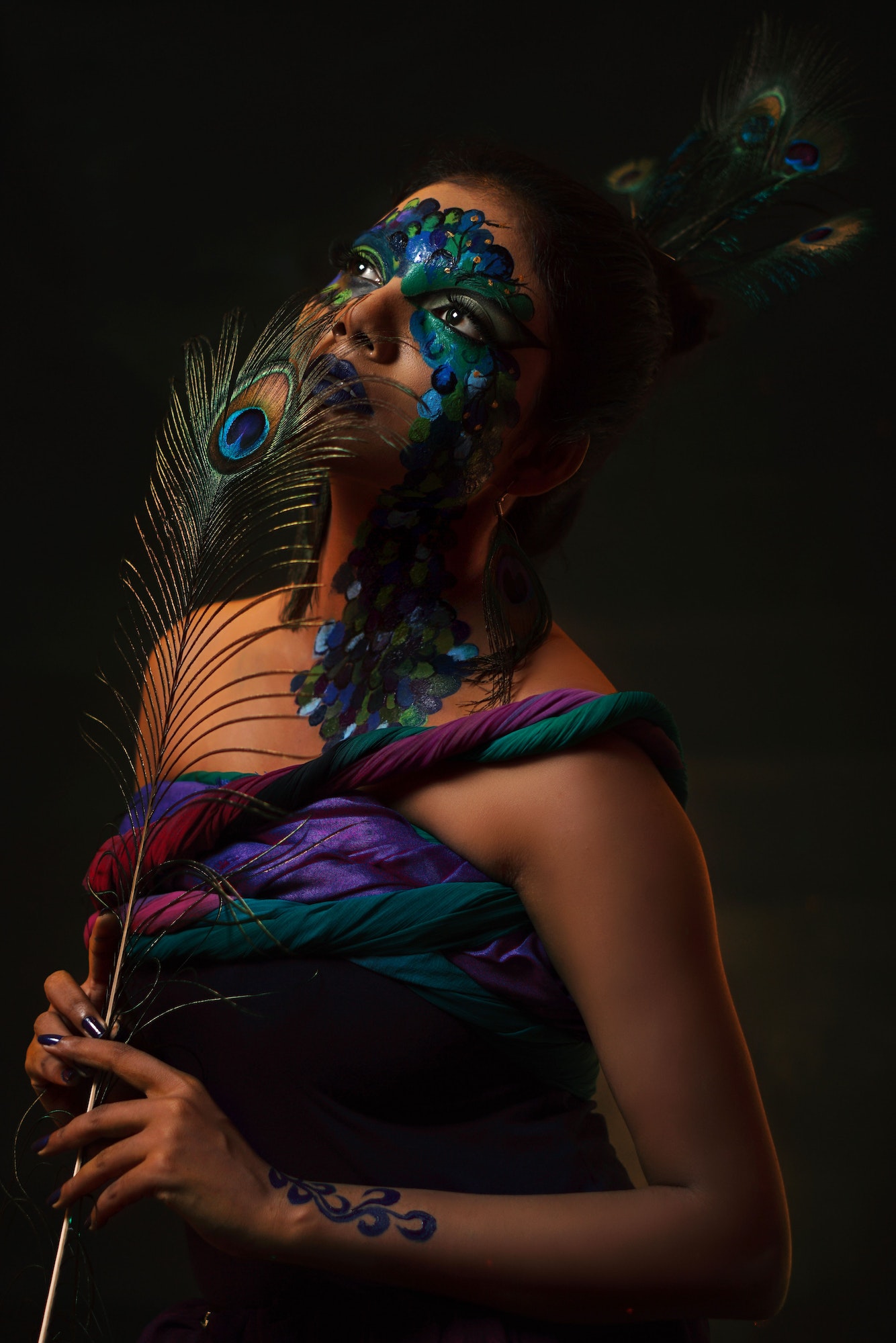 Southeast Asian young female with peacock style face painting and cloths on a black background