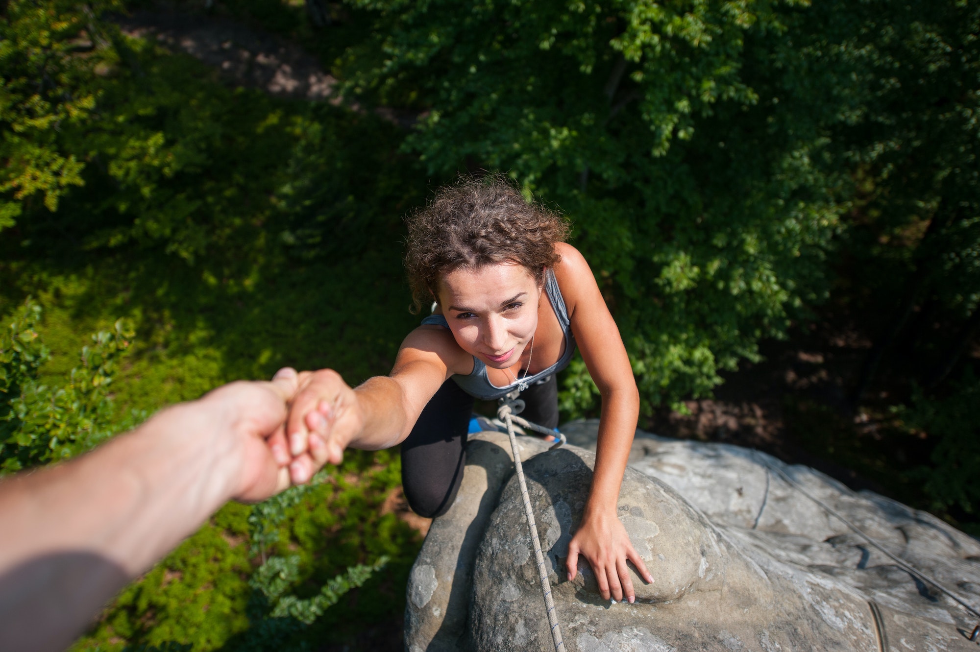 Woman climbing on large boulder, her partner giving her hand